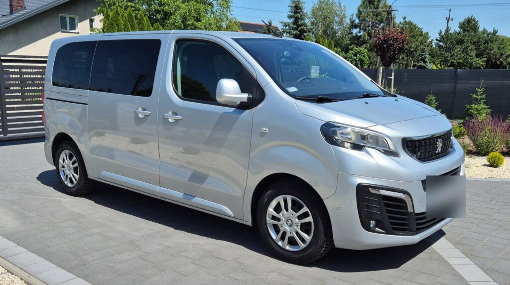 Srebrny bus osobowy Peugeot Traveller na podjeździe przed domem, tablica rejestracyjna zasłonięta