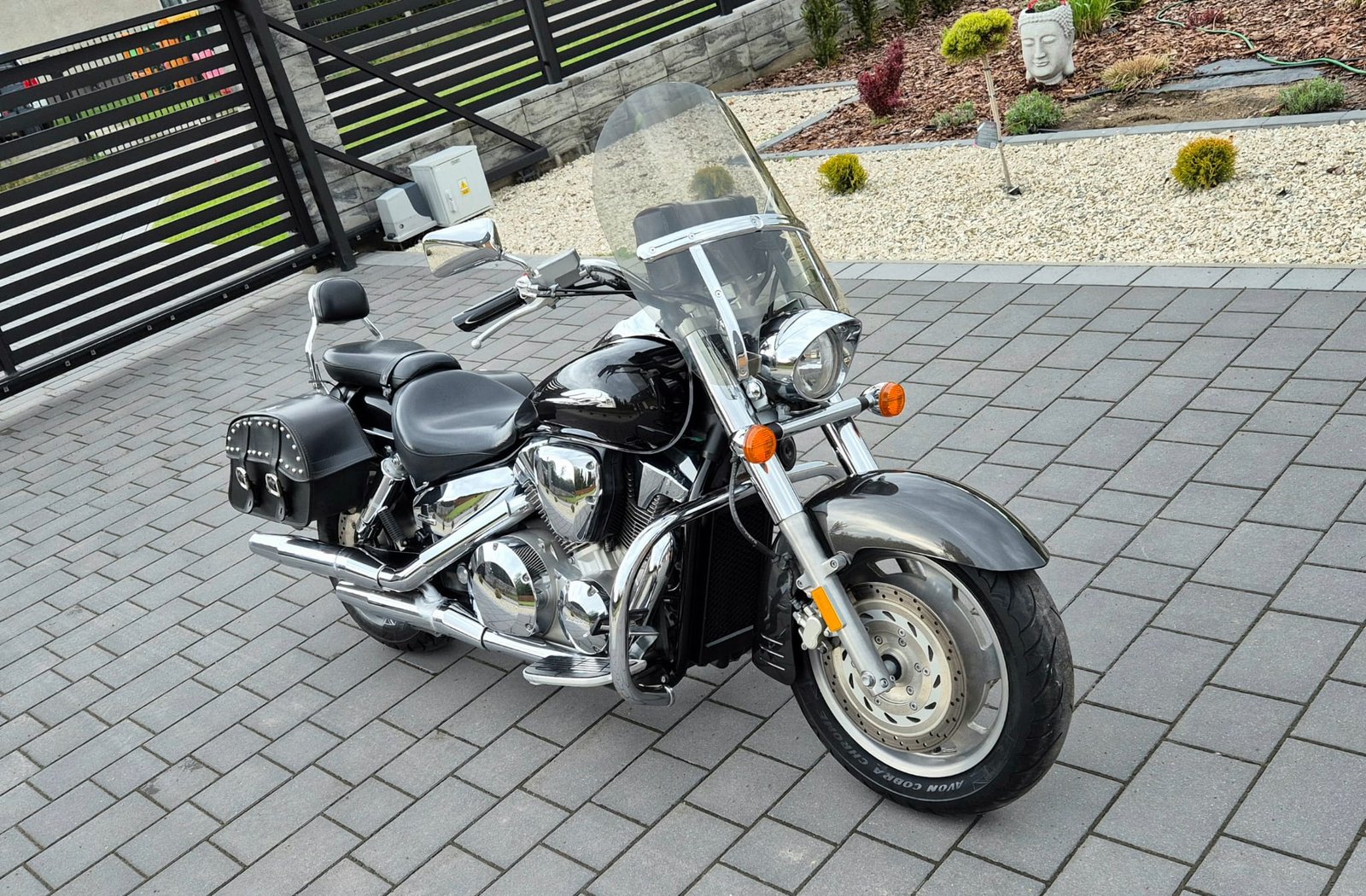 Czarna Honda VTX 1800 z sakwami i szybą na podjeździe z kostki brukowej