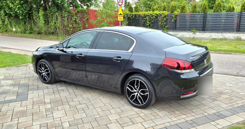 Grafitowy Peugeot 508 sedan zaparkowany na kostce przed posesją, widok z boku