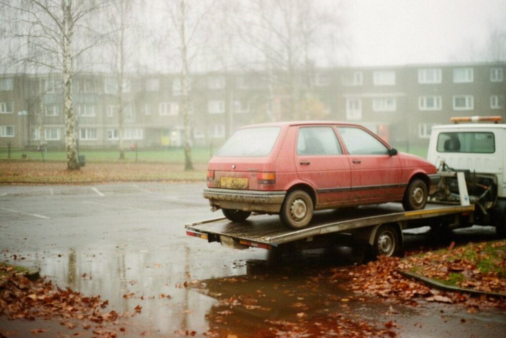 Stary czerwony hatchback na lawecie na mokrym parkingu osiedlowym jesienią