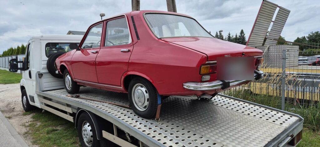 Czerwona Dacia 1300 zabezpieczona pasami na lawecie po odbiorze od sprzedającego
